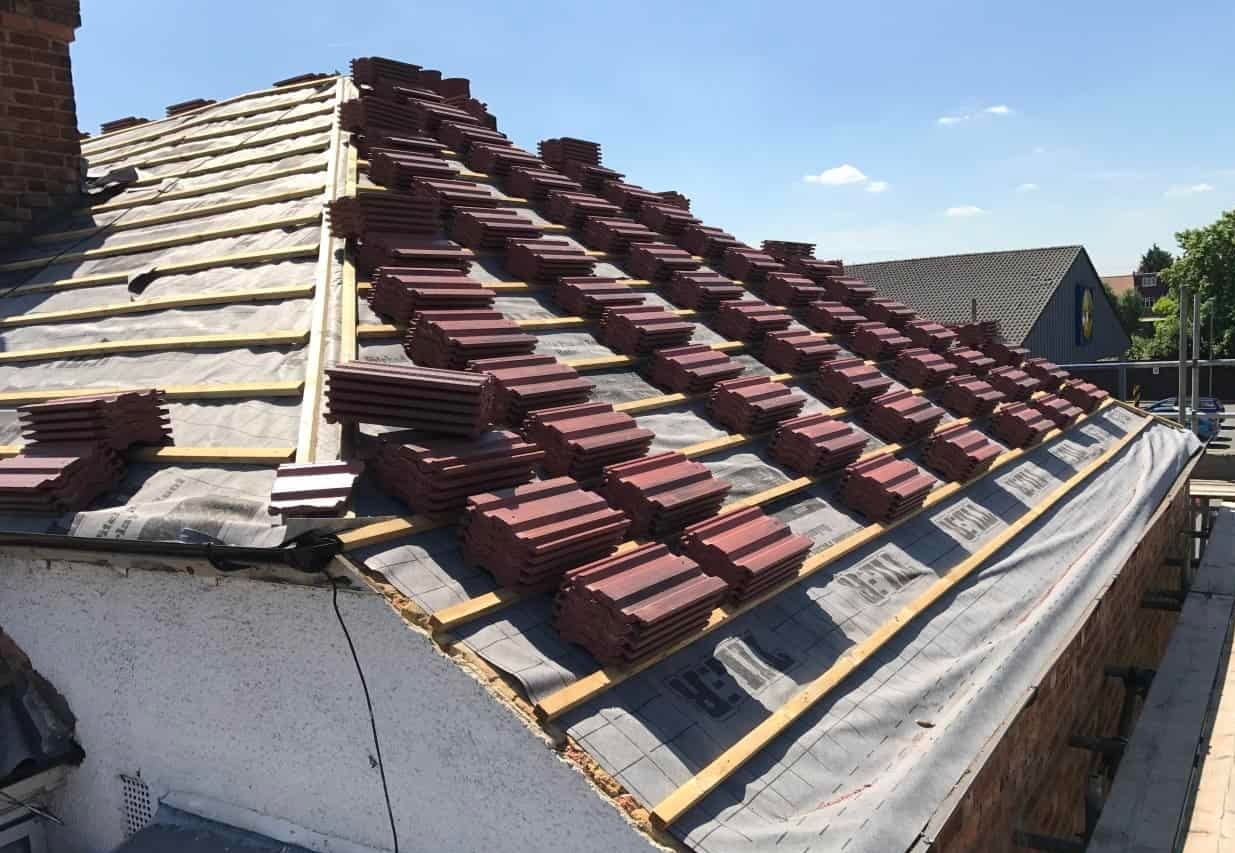 Re-roof in progress with new tiles stacked on battens beside a chimney stack